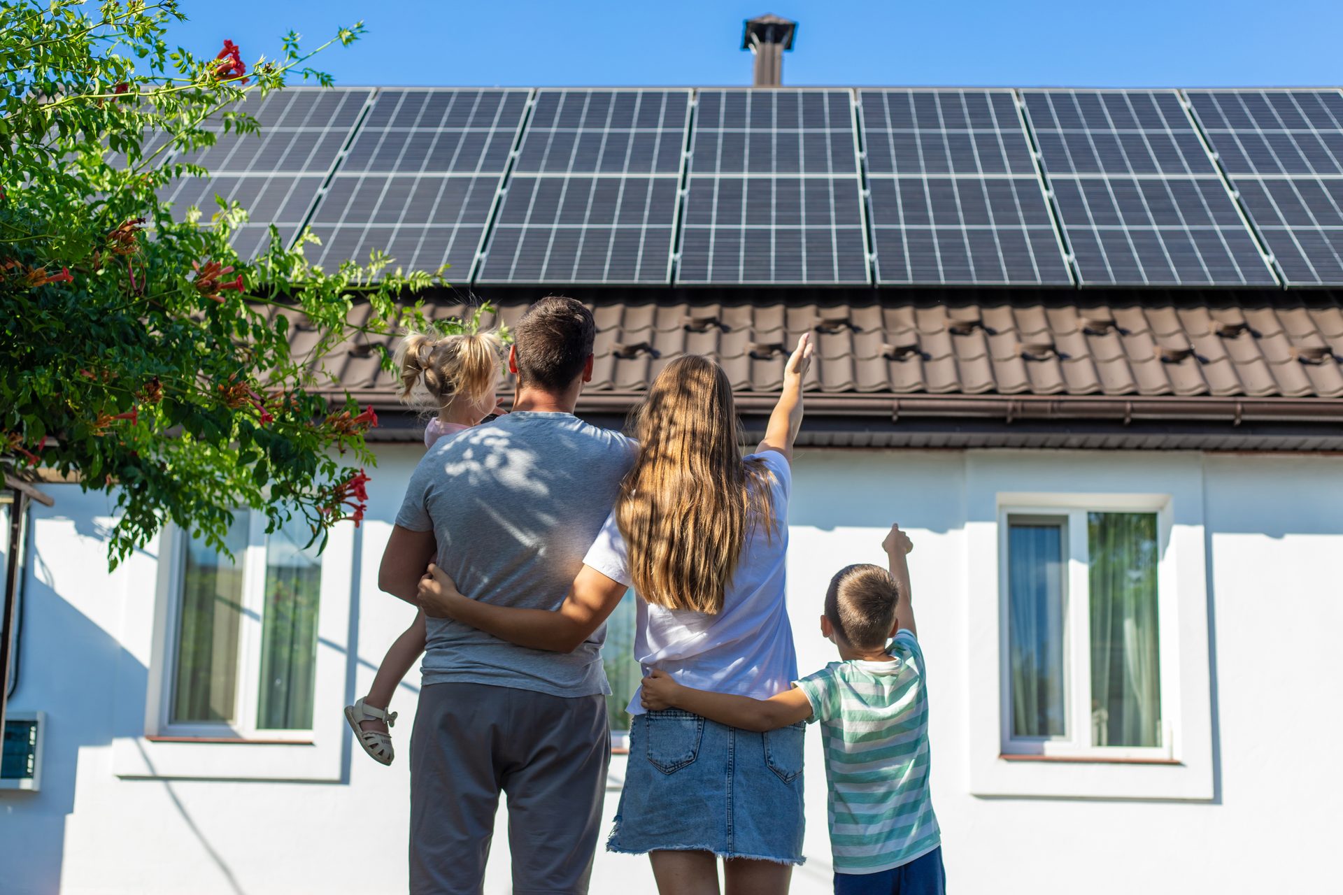 Family standing outside their home, pointing up at new rooftop solar panels