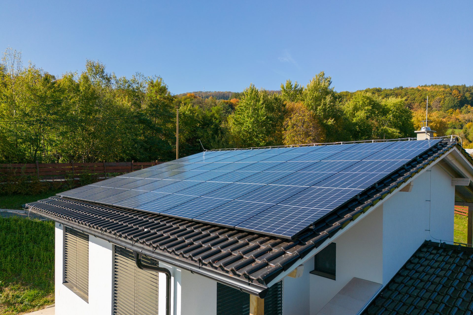 High-angle view of a rooftop solar array with trees beyond